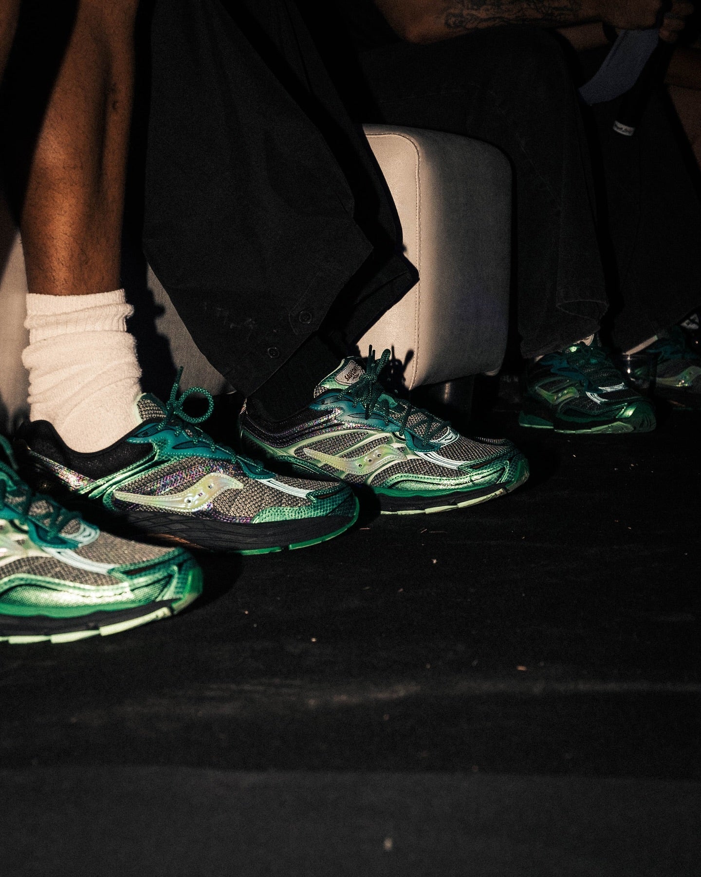 Kelių žmonių kojos su Saucony sportbačiais, matomas batų dizainas.